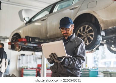 young serviceman checking car diagnostics with a laptop, car in the background medium shot. High quality photo - Powered by Shutterstock