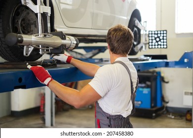 Young Serviceman Checking Wheel Alignment  In A Car Workshop 