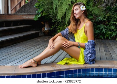 young sexy beautiful woman sitting by the pool, summer vacation, resort hotel in thailand, slim, tanned skin, long legs, yellow dress, tropical style, smiling, sensual, romantic