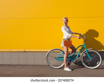 Young sexy blonde girl is standing near the vintage green bicycle with brown vintage bag