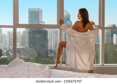 young sexy blonde standing topless near bedroom window dropping off her bathrobe and smiling