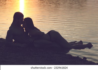 Young sexy couple on beach topless at sunset.Silhouette couple kissing over sunset background Fashion colors.