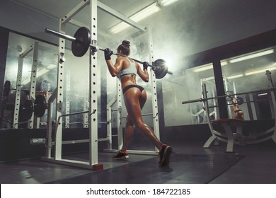 Young Sexy Girl In The Gym Doing Squat On Smoke Background