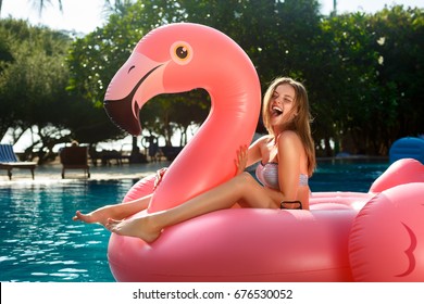 Young and sexy girl having fun and laughing on an inflatable giant pink flamingo pool float mattress in a bathing suit. Attractive tanned woman lies in the sun on vacation on Maldives
