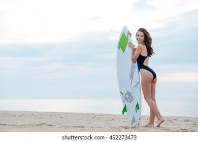 Young sexy girl standing on the beach holding a surfboard