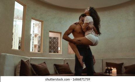 Young sexy man holding his girlfriend and kissing before having sex. Candles and glasses of wine on the table. Lovers enjoying foreplay, prelude before making love. Horizontal shot