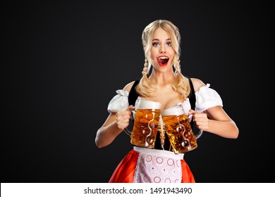 Young sexy oktoberfest girl waitress, wearing a traditional Bavarian or german dirndl, serving two big beer mugs with drink isolated on black background.