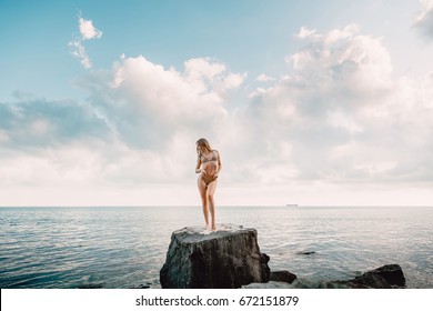 Young sexy woman in bikini swimsuit on stone and sea with sky, tropical island, summer vacation