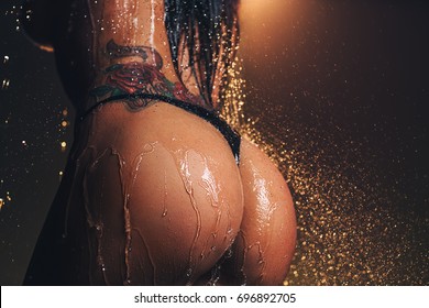 Young sexy woman butt with raining water. Tattoo on body.