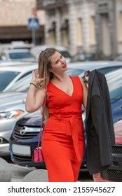 Young Sexy Woman With Curvy Body Shape Standing On Street And Car Background Wearing Red Close Fitting Sleeveless Dress With Deep Neckline