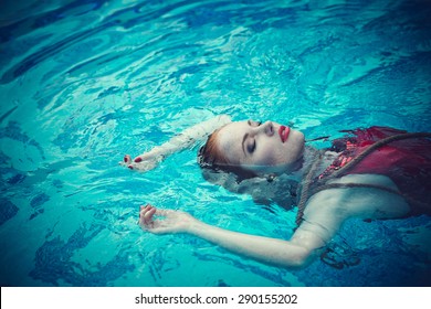 Young sexy woman floating on swimming pool in red dress. Beautiful rich lady who was strangled and thrown off into the water 