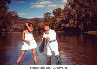 Young sexy woman and old fisherman standing in river with fishing rod. Father and daughter fishing. Mature rich businessman fisherman in suit with fishing rod, spinning reel on river.