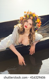 Young sexy woman on boat at sunset. The girl has a flower wreath on her head, relaxing and seiling on river. Beautiful body and face. Fantasy art photography. Concept of female beauty, rest in the