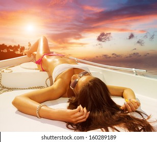 Young sexy woman on her private yacht at sunset