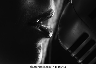 young sexy woman profile with pretty face and lips singing into studio silver microphone with long hair, closeup, black and white