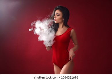 Young sexy woman in red body is vaping. A cloud of vapor. Studio shooting.