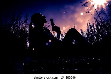 Young Sexy Woman Sitting With Gun In Her Hand. Black Silhouette Of Gangsta Woman On Dramatic Sky Background. 