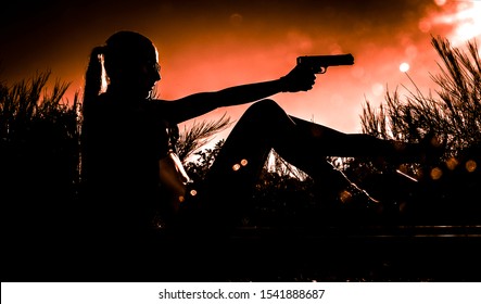 Young Sexy Woman Sitting With Gun In Her Hand. Black Silhouette Of Gangsta Woman On Dramatic Sky Background. 