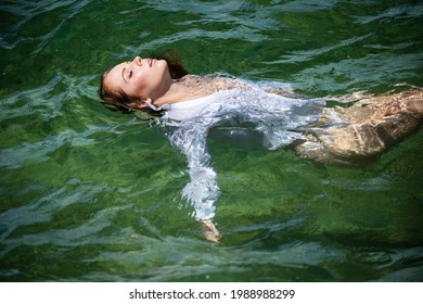 Young sexy woman is swimming in the transparent, blue sea. Sensual slim woman floating on the water of ocean water.