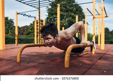 Young Shirtless Man Bodybuilder Doing Push-ups On A Parallel Bars During His Workout In A Modern Calisthenics Street Workout Park