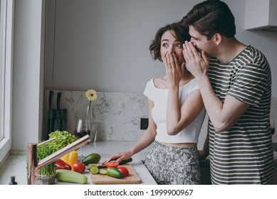 Young shock couple two woman man 20s in casual clothes boyfriend whisper gossip and tells secret behind his hand sharing news cook food in light kitchen at home together Healthy diet lifestyle concept