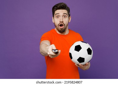 Young Shocked Astonished Surprised Fan Man He Wearing Orange T-shirt Cheer Up Support Football Sport Team Hold Soccer Ball Remote Controller Watch Tv Live Stream Isolated On Plain Purple Background