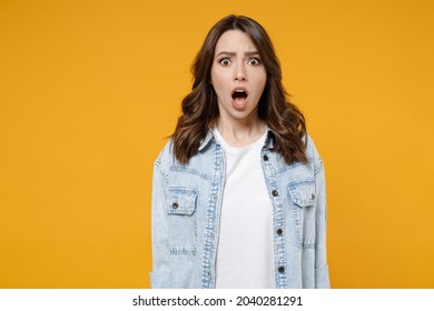 Young shocked confused wondered astonished indignant woman 20s wearing stylish casual denim shirt white t-shirt looking camera with opened mouth isolated on yellow color background studio portrait.