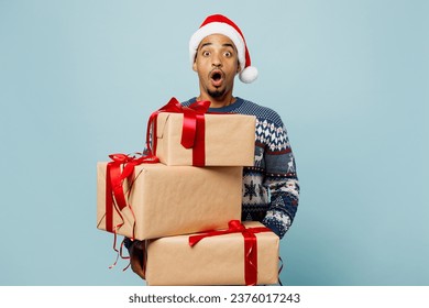 Young shocked fun man wears sweater Santa hat posing hold stack of present box with gift ribbon bow isolated on plain pastel blue background. Happy New Year 2024 celebration Christmas holiday concept - Powered by Shutterstock