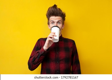 Young Shocked Guy Drinks Invigorating Coffee And Is Surprised At A Yellow Isolated Background, A Man Drinks An Energy Drink