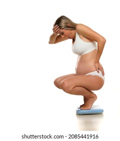 Young Shocked Pregnant Woman In A Crouching Position On A Scale On A White Background