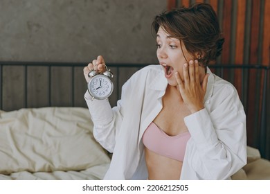 Young shocked sad woman wear white shirt pajama she lying in bed being late hold face look at clock alarm rest relax spend time in bedroom lounge home in own room hotel wake up. Real estate concept - Shutterstock ID 2206212505