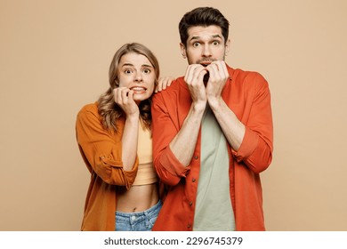 Young shocked scared fearful couple two friends family man woman wear casual clothes looking camera biting nails fingers together isolated on pastel plain light beige color background studio portrait