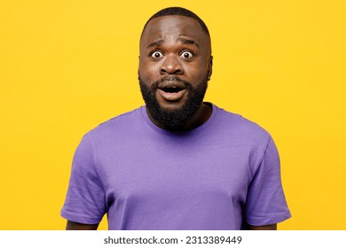 Young shocked scared sad man of African American ethnicity he wear casual clothes purple t-shirt look camera with opened mouth isolated on plain yellow background studio portrait. Lifestyle concept