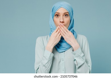 Young shocked surprised astonished arabian asian muslim woman in abaya hijab cover mouth with hand isolated on plain blue background studio portrait. People uae middle eastern islam religious concept