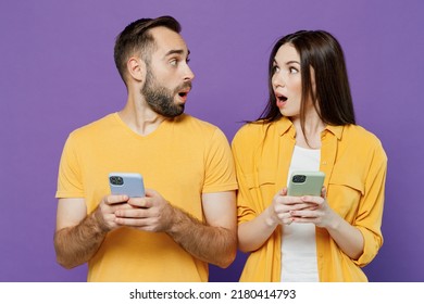 Young Shocked Surprised Couple Two Friends Family Man Woman Together In Yellow Casual Clothes Hold In Hand Use Mobile Cell Phone Chatting Look To Each Other Isolated On Plain Violet Background Studio