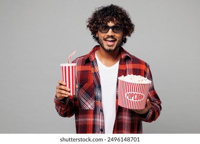 Young shocked surprised happy Indian man wear red shirt casual clothes 3d glasses watch movie film hold bucket of popcorn cup of soda pop in cinema isolated on plain grey background studio portrait - Powered by Shutterstock