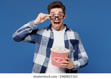 Young shocked surprised man he wear shirt white t-shirt casual clothes lower 3d glasses watch movie film hold bucket of popcorn in cinema look camera isolated on plain blue background studio portrait - Powered by Shutterstock