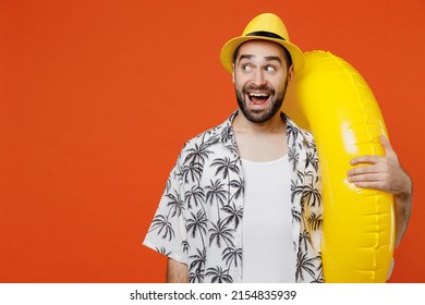 Young shocked surprised tourist man wear beach shirt hat hold inflatable ring look aside on workspace area isolated on plain orange background studio portrait. Summer vacation sea rest sun tan concept