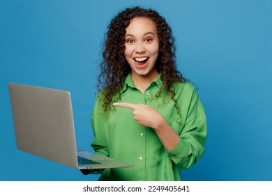 Young shocked IT woman of African American ethnicity 20s she wear green shirt hold use work point index finger on laptop pc computer isolated on plain blue background studio. People lifestyle concept - Powered by Shutterstock