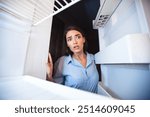 Young shocked woman looking in empty fridge at home, view from inside