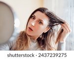 Young shocked woman is surprised to see dirty oily and greasy hair looking in mirror at home. Health treatment. Hair care products. Selfcare