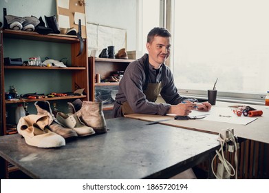 A young shoemaker makes a drawing for a pattern for leather shoes on a table in his workshop.