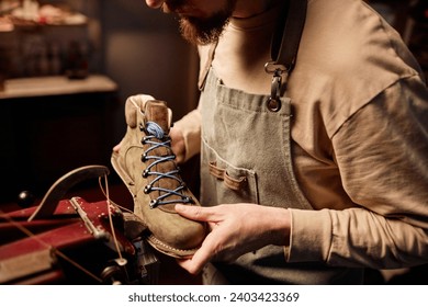 Young shoemaking master sewing upper part of boot workpiece together with sole