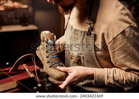 Young shoemaking master sewing upper part of boot workpiece together with sole