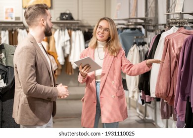 Young Shop Assistant Using Digital Tablet And Consulting Customer In The Clothing Shop