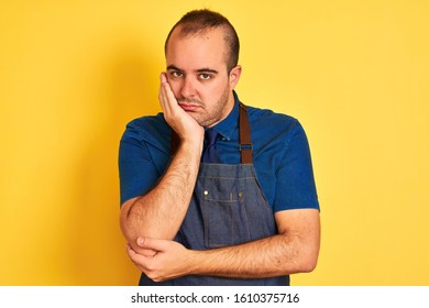 Young Shopkeeper Man Wearing Apron Standing Over Isolated Yellow Background Thinking Looking Tired And Bored With Depression Problems With Crossed Arms.