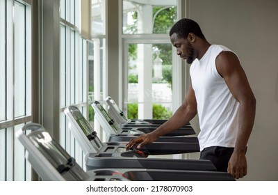 Young Short Curly Black Hair Man With Moustache And Beard Selecting Running Program On Treadmill In The Gym.