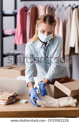 young showroom owner in medical mask, packing clothes into boxes