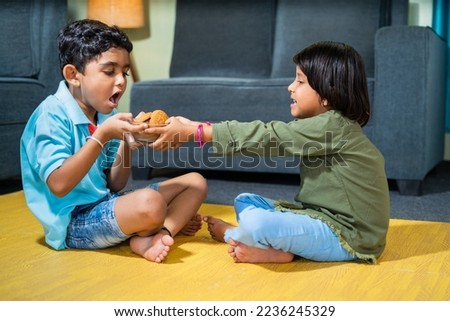 Young siblings kids fighting for snacks or biscuit while sitting on floor at home - concept of childhood lifestyle, relationships and weekend holidays
