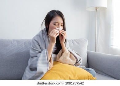 Young Sick Asian Woman Sitting under the Blanket Whiles Sneezing  with Tissue on the Sofa - Shutterstock ID 2081939542